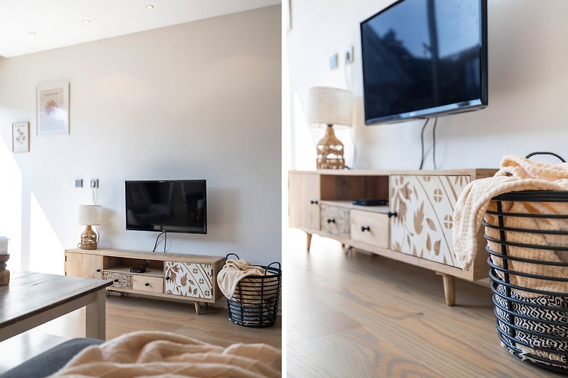 Comfortabele woonkamer met grijze bank, houten meubels en televisie.