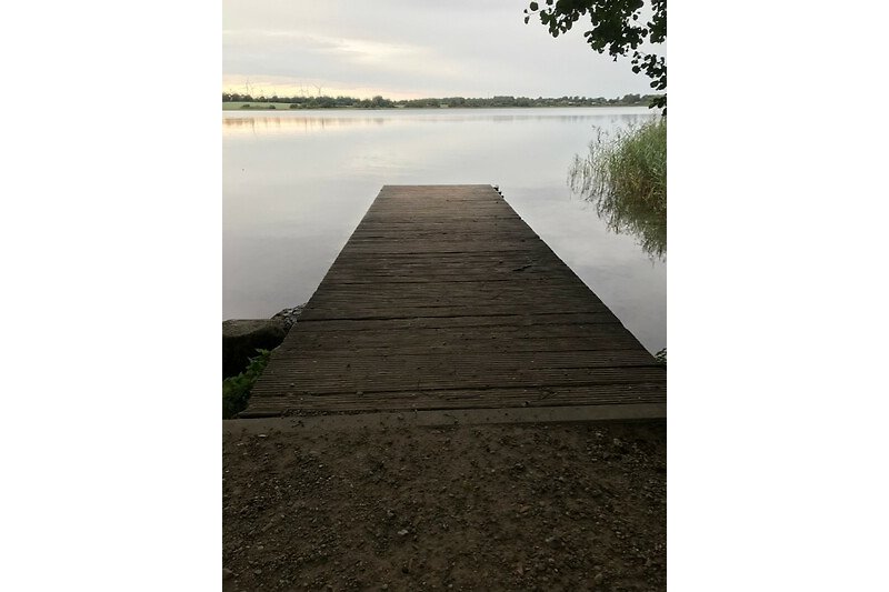 Ein ruhiger See mit einem Holzsteg und einer malerischen Landschaft.