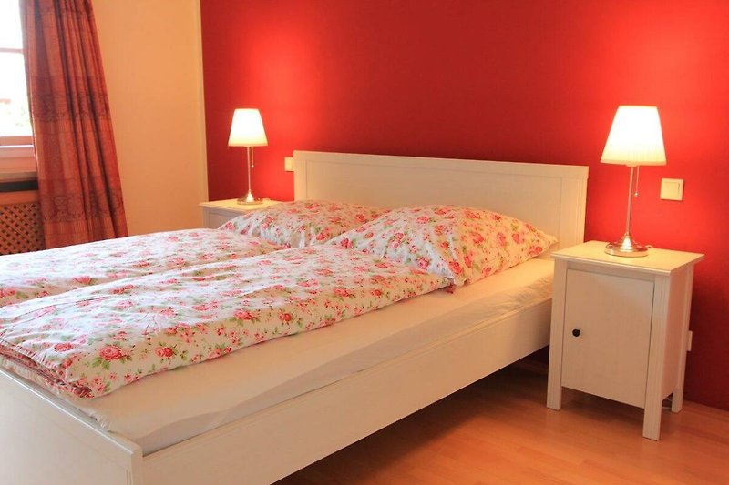 Gemütliches Schlafzimmer mit rotem Bett, Holzboden und stilvoller Inneneinrichtung.
