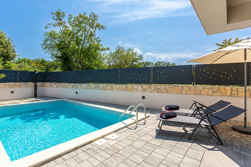 A modern villa with a swimming pool, deckchairs and a shady area for relaxation.