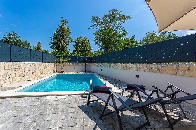 Moderne Villa mit Swimmingpool, Solardusche im Freien, Liegestühlen und einem schattigen Bereich zum Entspannen.