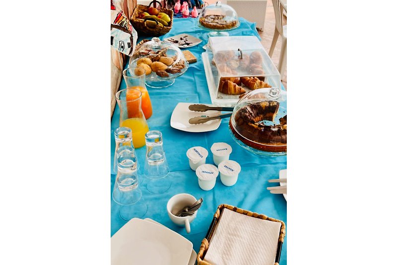Una tavola apparecchiata con piatti, bicchieri e tazze, circondata da un ambiente verde e blu.