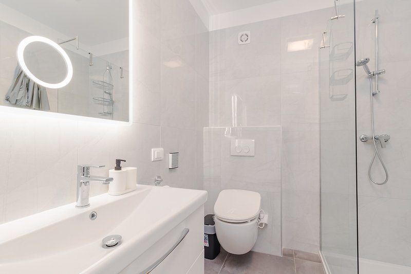 Moderan kupaonski prostor s bijelim umivaonikom, tušem i ogledalom.