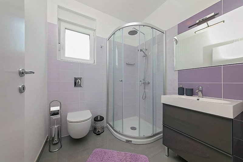 Udobna kupaonica s modernim tušem i staklenim vratima.