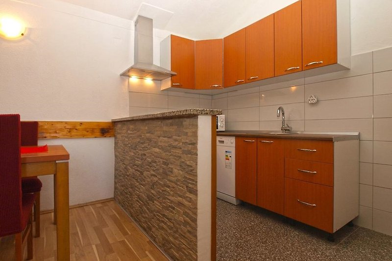 Drvena kuhinja s kuhinjskim elementima i narančastim detaljima.