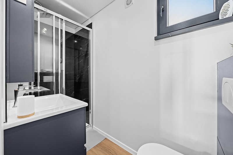 Moderan interijer kupaonice s metalnim slavinama i staklenim umivaonikom.