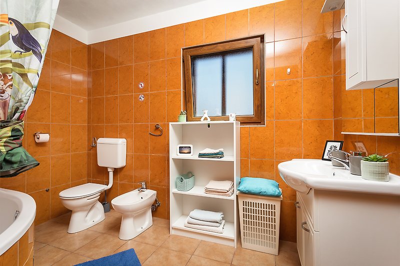 Udobna kupaonica s narančastim detaljima i keramičkim umivaonikom.