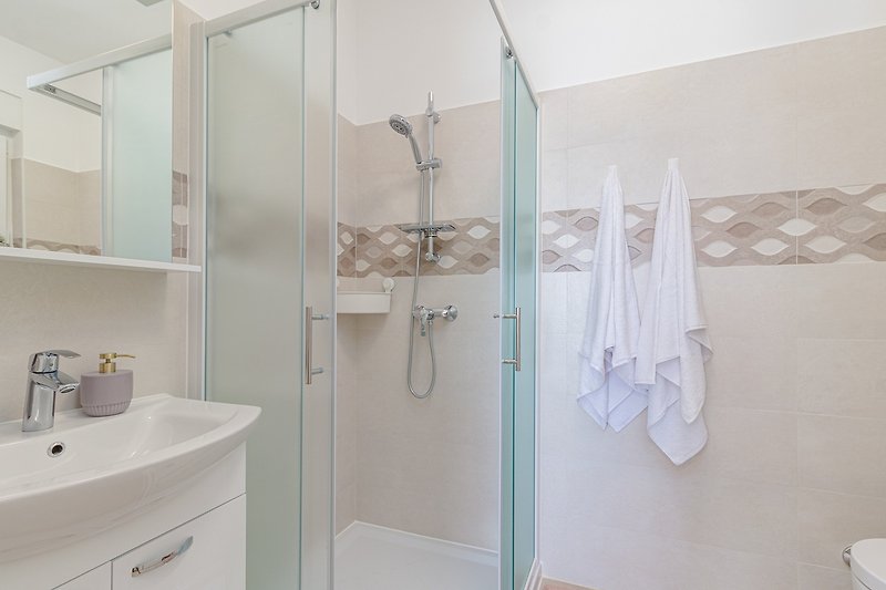 Moderan kupaonski prostor s ogledalom, umivaonikom i tušem.