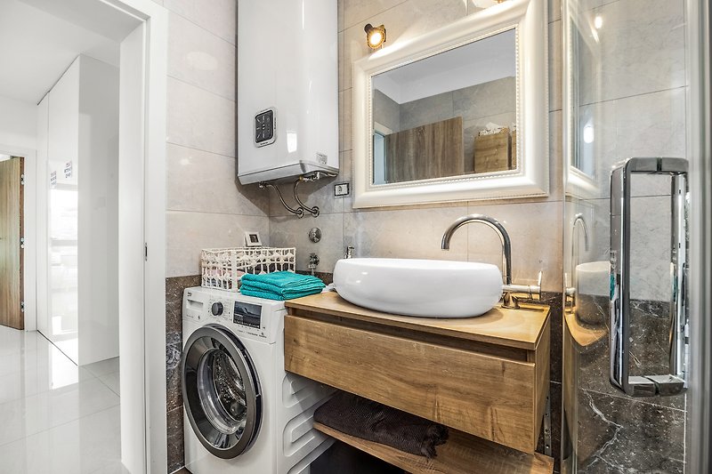 Moderan kupaonski prostor s ogledalom, umivaonikom i drvenim ormarićem.