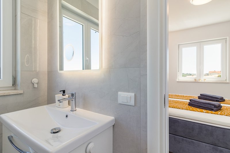 Moderan kupaonski prostor s ogledalom, umivaonikom i slavinom.