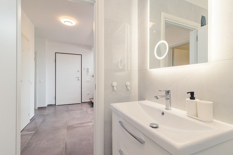 Moderan kupaonski prostor s ogledalom, umivaonikom i slavinom.