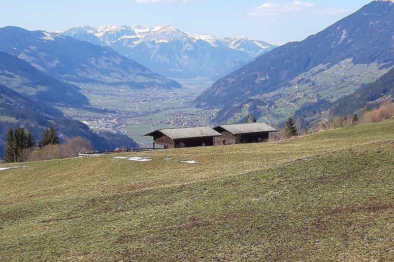 Bergiges Panorama mit grünen Wiesen, Schnee und Hütte.