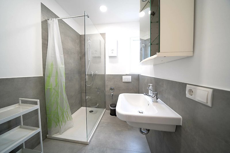 Moderne Badezimmerausstattung mit Spiegel, Waschbecken und Dusche.