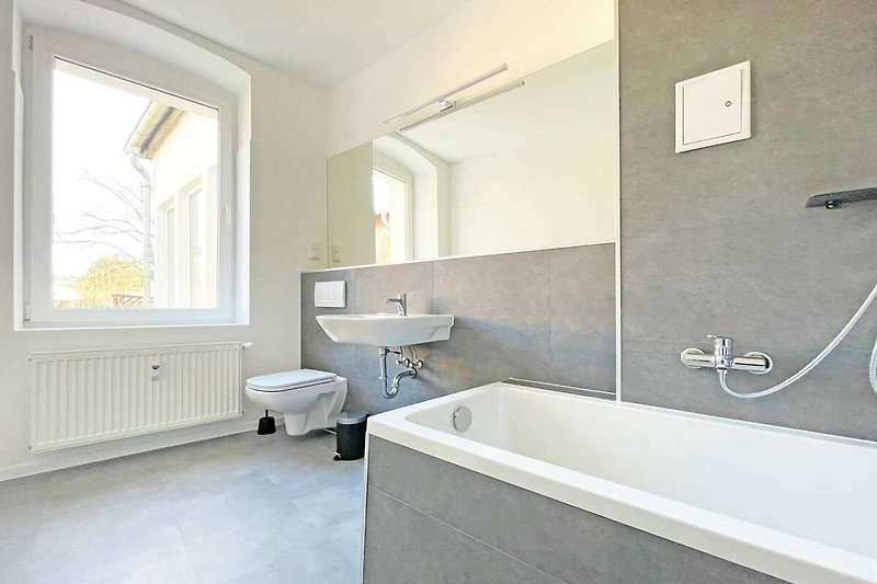 Schönes Badezimmer mit Badewanne, Spiegel und Fenster.