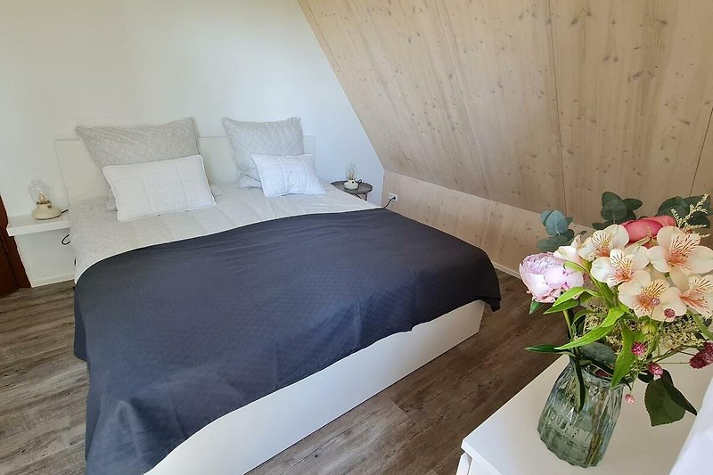 Gemütliches Schlafzimmer mit bequemem Bett, Holzmöbeln und Blumen.