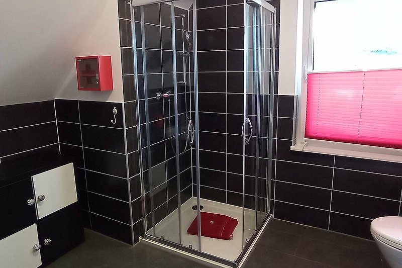 Moderne Badezimmerausstattung mit roten Akzenten und Fenster. Perfekt für Ihren Urlaub!