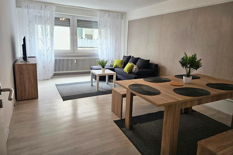 Helles Wohnzimmer mit Holzlaminat, großen Fenstern und Pflanzen.