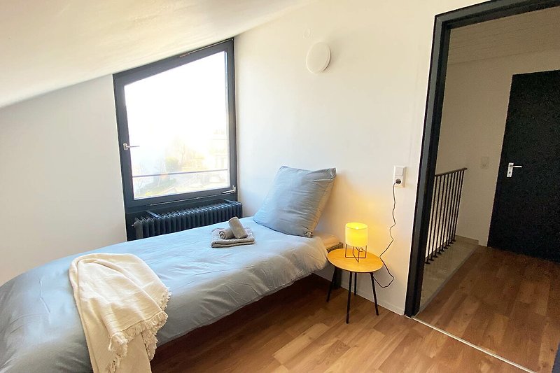 Gemütliches Schlafzimmer mit Fenster, Holzbett und gemütlicher Beleuchtung.
