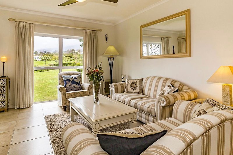 Gemütliches Wohnzimmer mit bequemer Couch, stilvoller Beleuchtung und Blick auf den Golfplatz