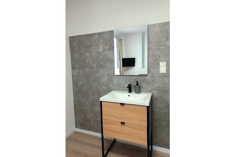 Modernes Badezimmer mit Spiegel, Wasserhahn und Waschbecken.