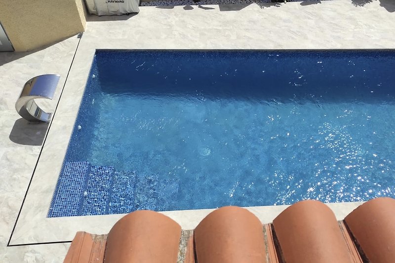 Schwimmbad mit türkisblauem Wasser und Sonnenliegen. Sicht vom Balkon des Studios
