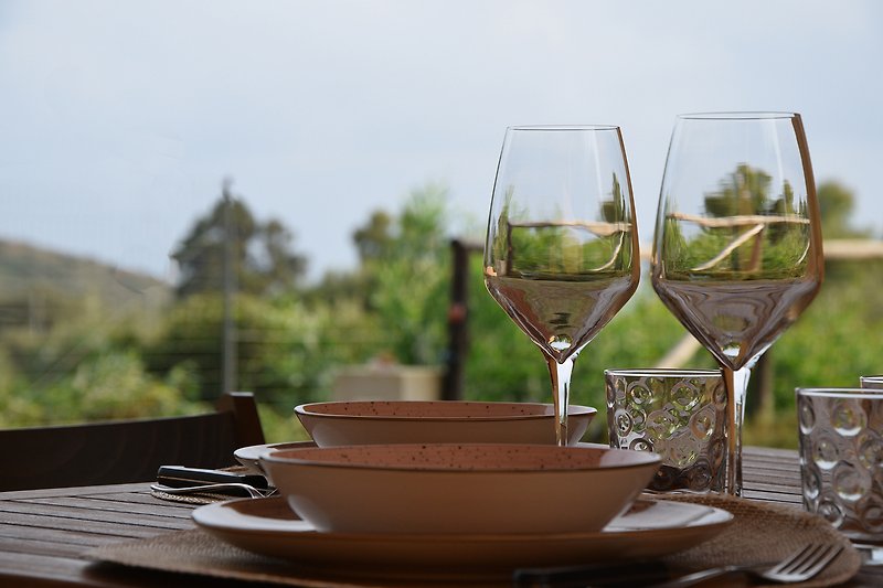 Una tavola apparecchiata con bicchieri di vino, circondata da alberi verdi e un prato curato.