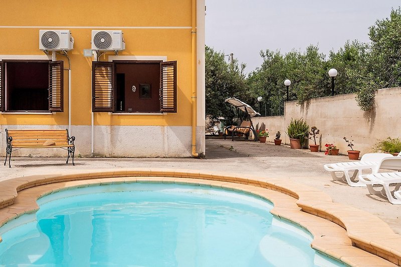 Una proprietà con una piscina azzurra, sedie all'ombra e una vista mozzafiato sul mare.