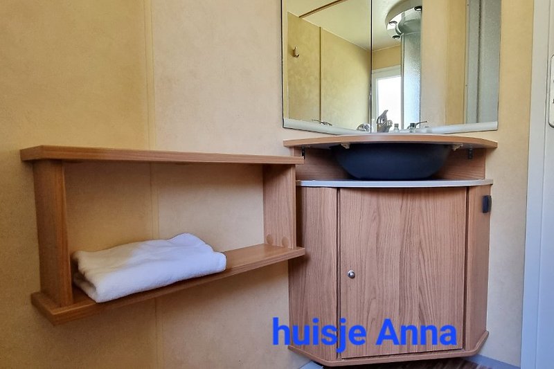 Badkamer met spiegel, wastafel, kastjes en houten accenten.