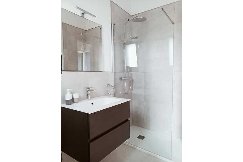 Stilvolles Badezimmer mit elegantem Spiegel, Waschbecken und begehbarer Dusche.
