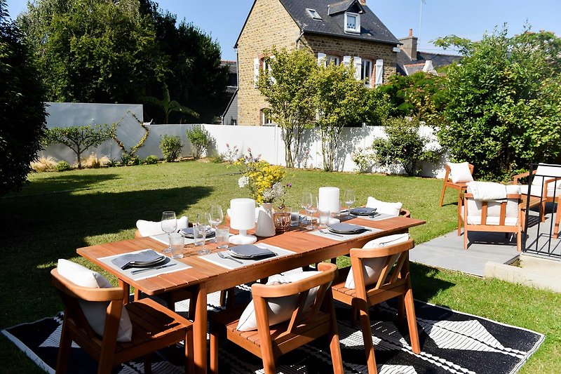Maison avec mobilier d'extérieur, table en bois et jardin verdoyant.