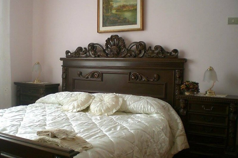 Camera da letto matrimoniale  con mobili in legno intagliati e comodo materasso.