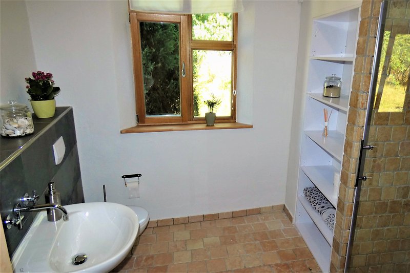 Gemütliches Badezimmer mit Fenster, Spiegel und Natursteinfliesen.