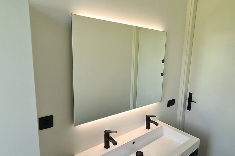Schönes Badezimmer mit Spiegel, Wasserhahn und Waschbecken.