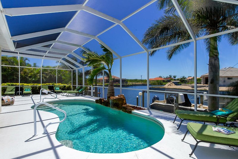 Schönes Haus mit Pool, Sonnenliegen und Palmen am Wasser.