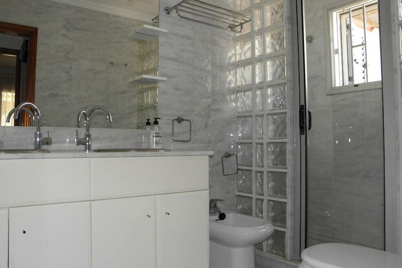 Badezimmer mit Doppelwaschbecken, Dusche und Toilette.