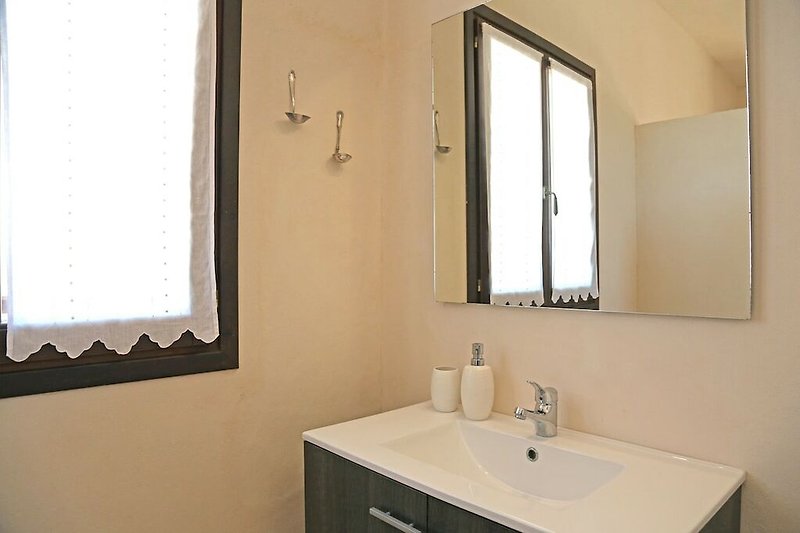 Espejo y lavabo en un baño con ventana y muebles de madera.