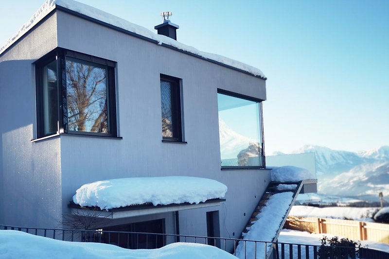 Winterliches Haus mit schneebedecktem Dach und Bergblick.