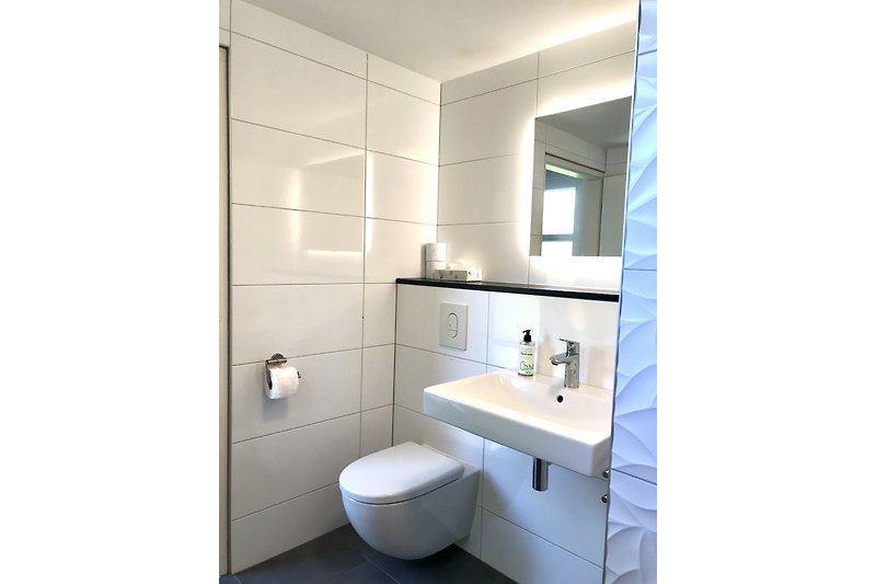 Ein modernes Badezimmer mit Spiegel (mit Licht), Waschbecken und WC.