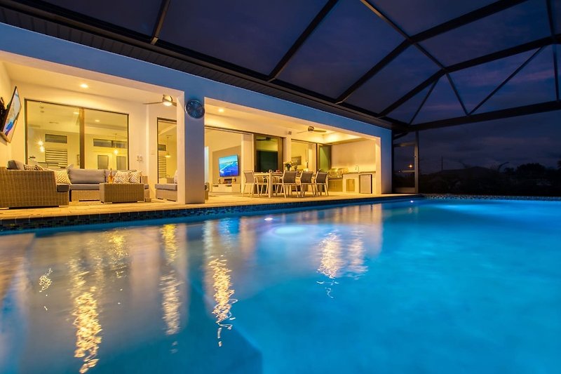 Schwimmbad mit Glasarchitektur, blauem Wasser und tropischer Umgebung.