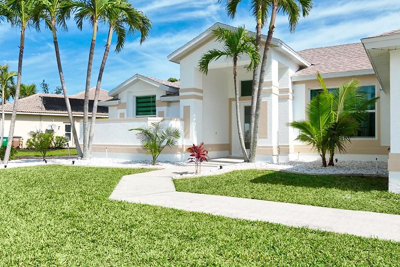 Schönes Haus mit grünem Garten und stilvoller Fassade, umgeben von Palmen und einer idyllischen Landschaft.