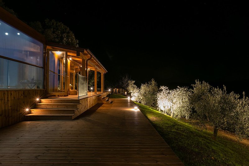 Una casa di legno con illuminazione notturna, circondata da alberi e un vialetto.
