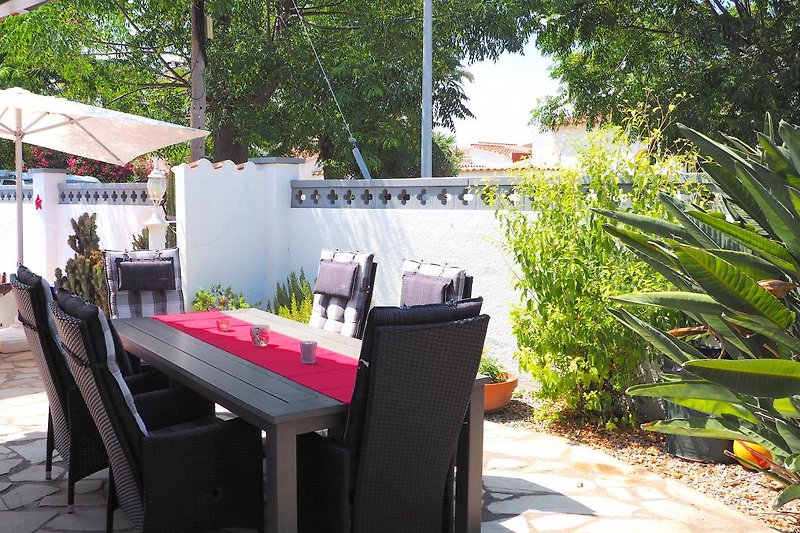 Gemütlicher Außenbereich mit Tisch, Stühlen, Sonnenschirm und Pflanzen.
