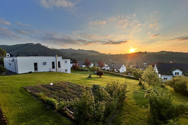 Ferienhaus mit Bergblick, grüner Wiese und malerischem Sonnenuntergang.