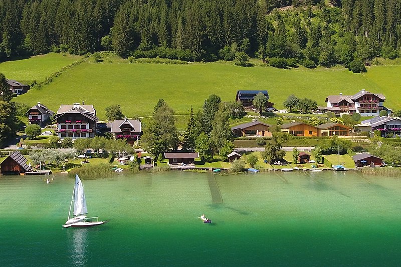 Ferienhaus mit See, Booten und grüner Landschaft.