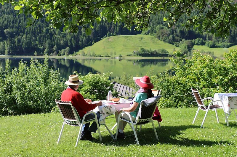 Eine grüne Oase am See mit Gartenmöbeln und entspannten Menschen.