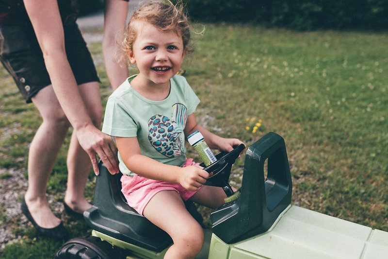 Familie mit glücklichem Kind spielt im Garten mit Spielzeugauto und lächelt.
