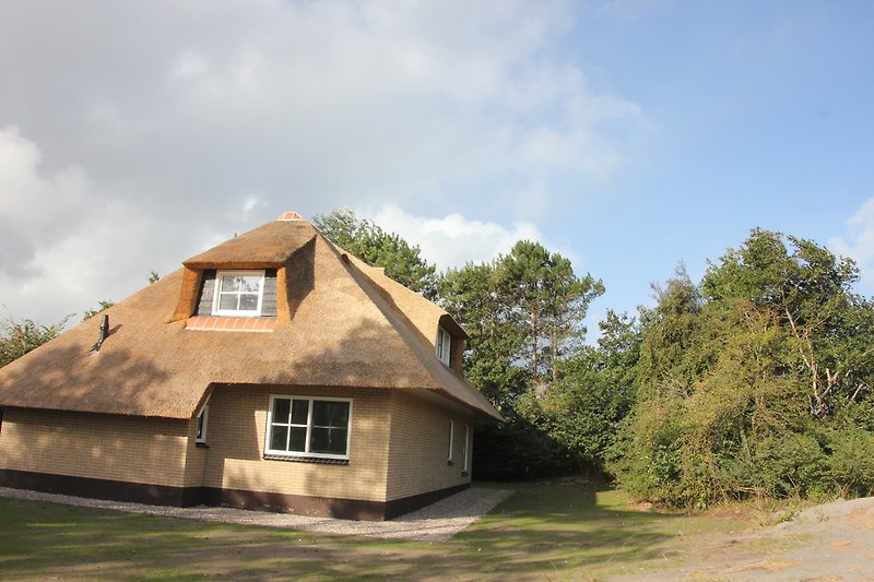 Schönes Ferienhaus mit thatched Dach, Holzverkleidung und Garten.