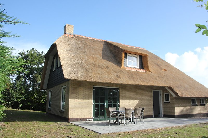 Schönes Ferienhaus mit thatched Dach, Holzverkleidung und Garten.