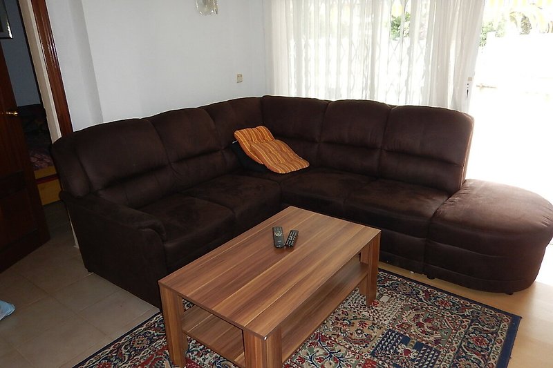 Gemütliches Wohnzimmer mit brauner Couch, Holzmöbeln und bequemem Tisch.