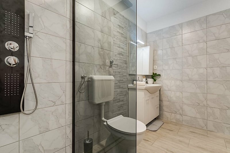 A modern bathroom with a grey sink, glass mirror, and ceramic tile flooring.